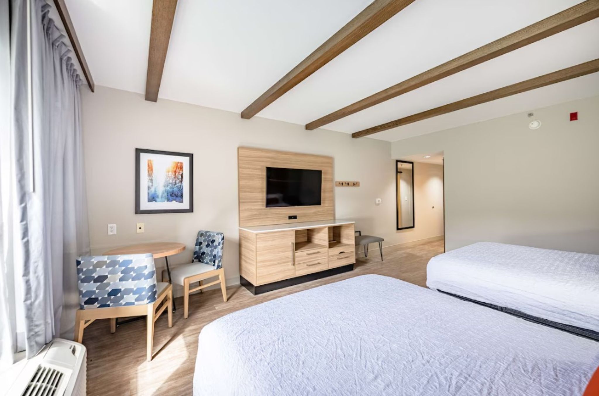 Une chambre d’hôtel avec un lit, une télévision, une petite table avec des chaises et une fenêtre avec des rideaux.