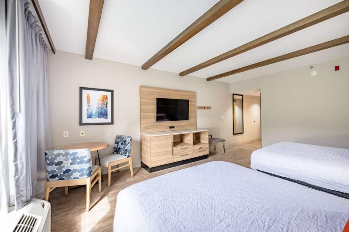 A hotel room with a bed, a TV, a small table with chairs, and a window with curtains.