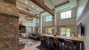 A spacious living area with a stone fireplace, high ceilings, and large windows. - Hampton Inn & Suites Cashiers Sapphire Valley (Sapphire)