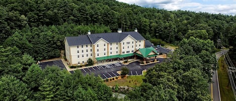 A large building surrounded by dense forest, with a parking lot and a covered walkway.