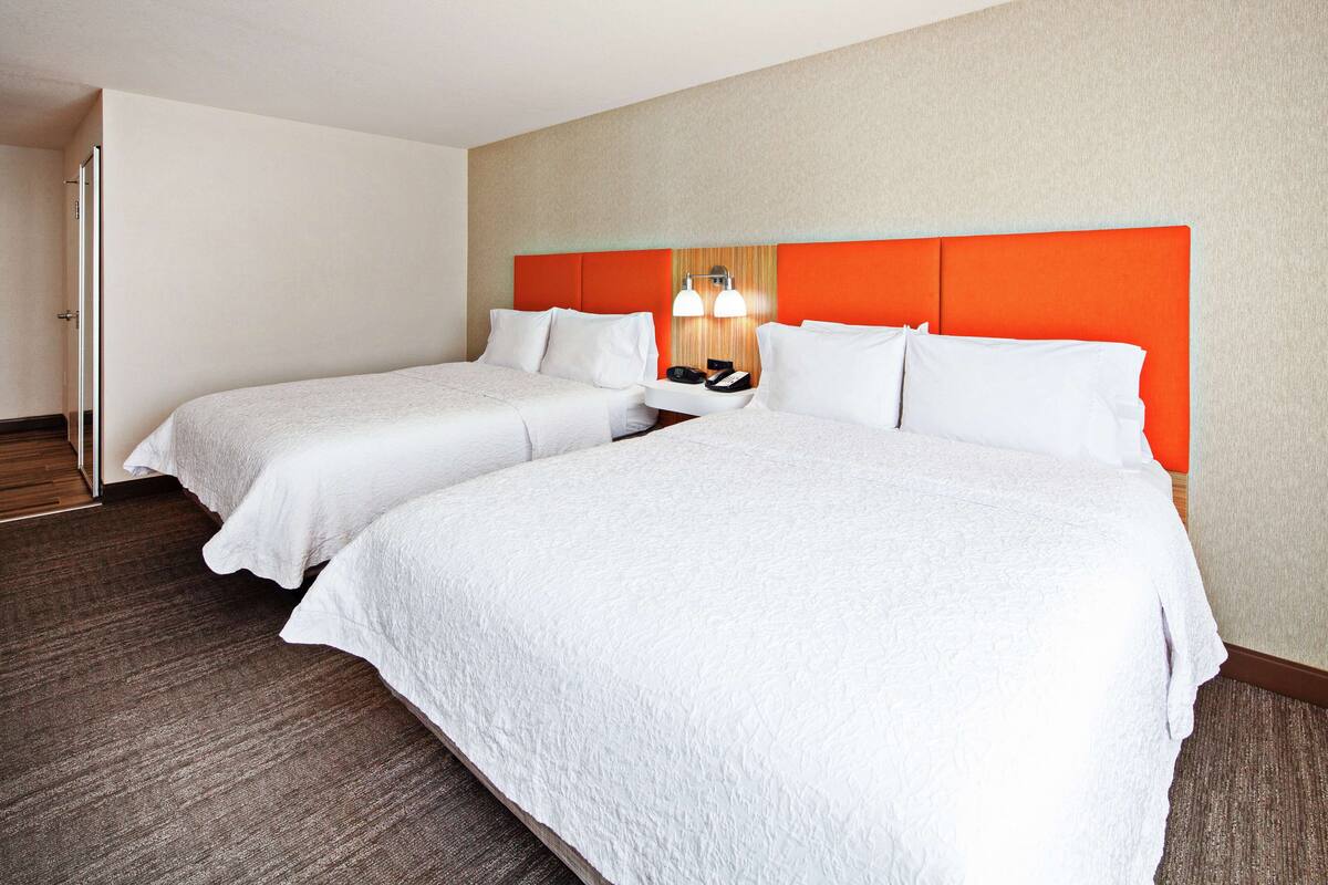 A hotel room with two beds, a wooden floor, and a beige wall.