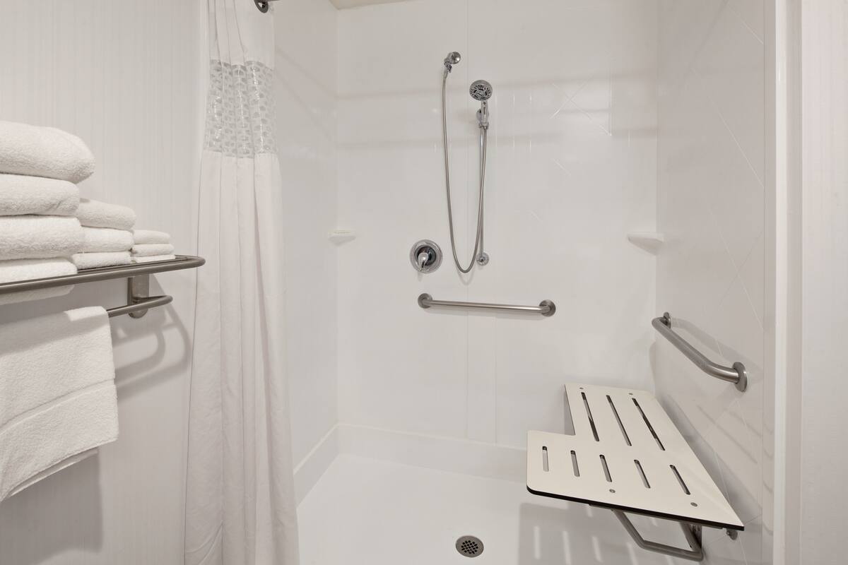 A shower area with a glass door, a towel rack with folded towels, a handheld showerhead, and a safety grab bar.