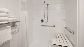 A shower area with a glass door, a towel rack with folded towels, a handheld showerhead, and a safety grab bar.