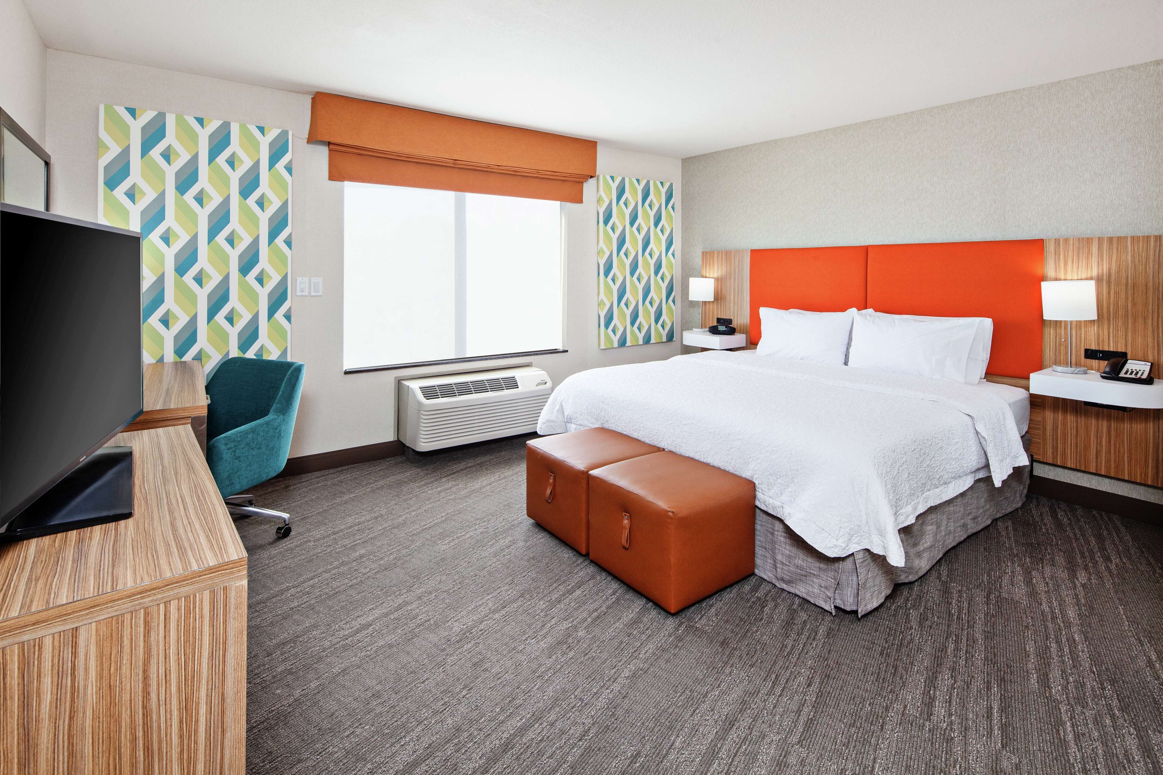 Une chambre d’hôtel comprenant un lit, une télévision, un bureau, une chaise, une fenêtre et un mur recouvert d’un papier peint à motifs.