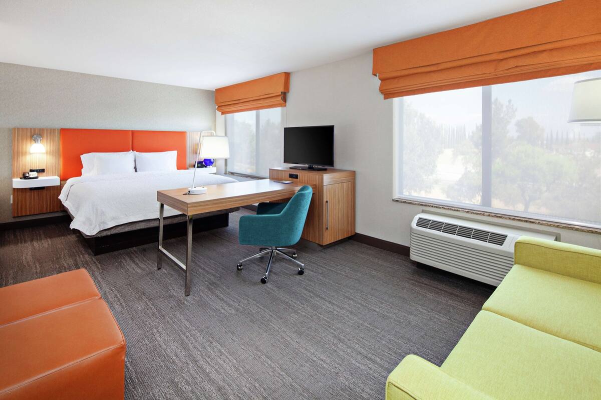 A hotel room with a bed, desk, chair, and a TV.