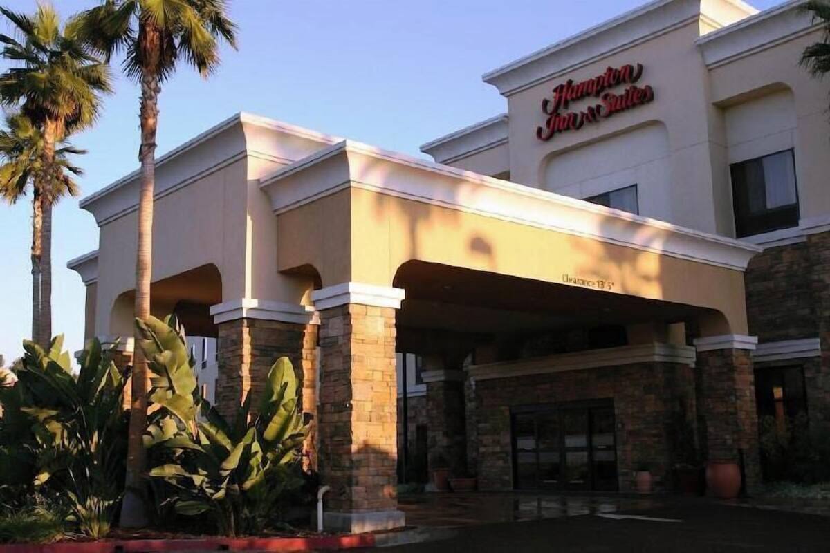 A hotel with a modern facade, palm trees, and a sign that reads 'Hampton Inn & Suites.'