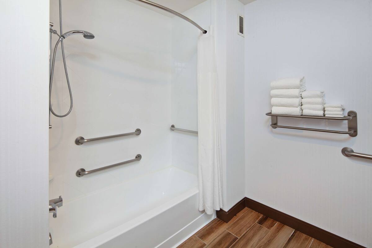 A bathroom with a shower, grab bars, a towel rack, and a wooden floor.