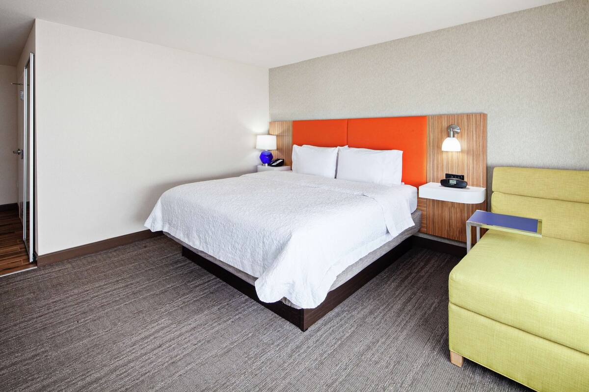 A hotel room with a bed, a nightstand, a lamp, and a chair.