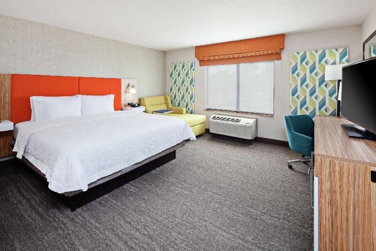 A hotel room with a bed, a desk, a chair, a TV, and a window.