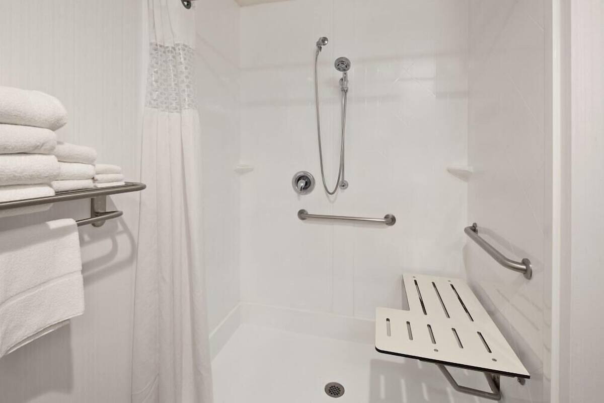 A shower with a handheld showerhead, a handheld showerhead, a grab bar, and a towel rack with folded towels.