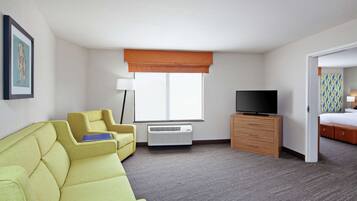 Une chambre d’hôtel avec un canapé vert, une télévision, une commode et une fenêtre donnant sur un beau paysage.
