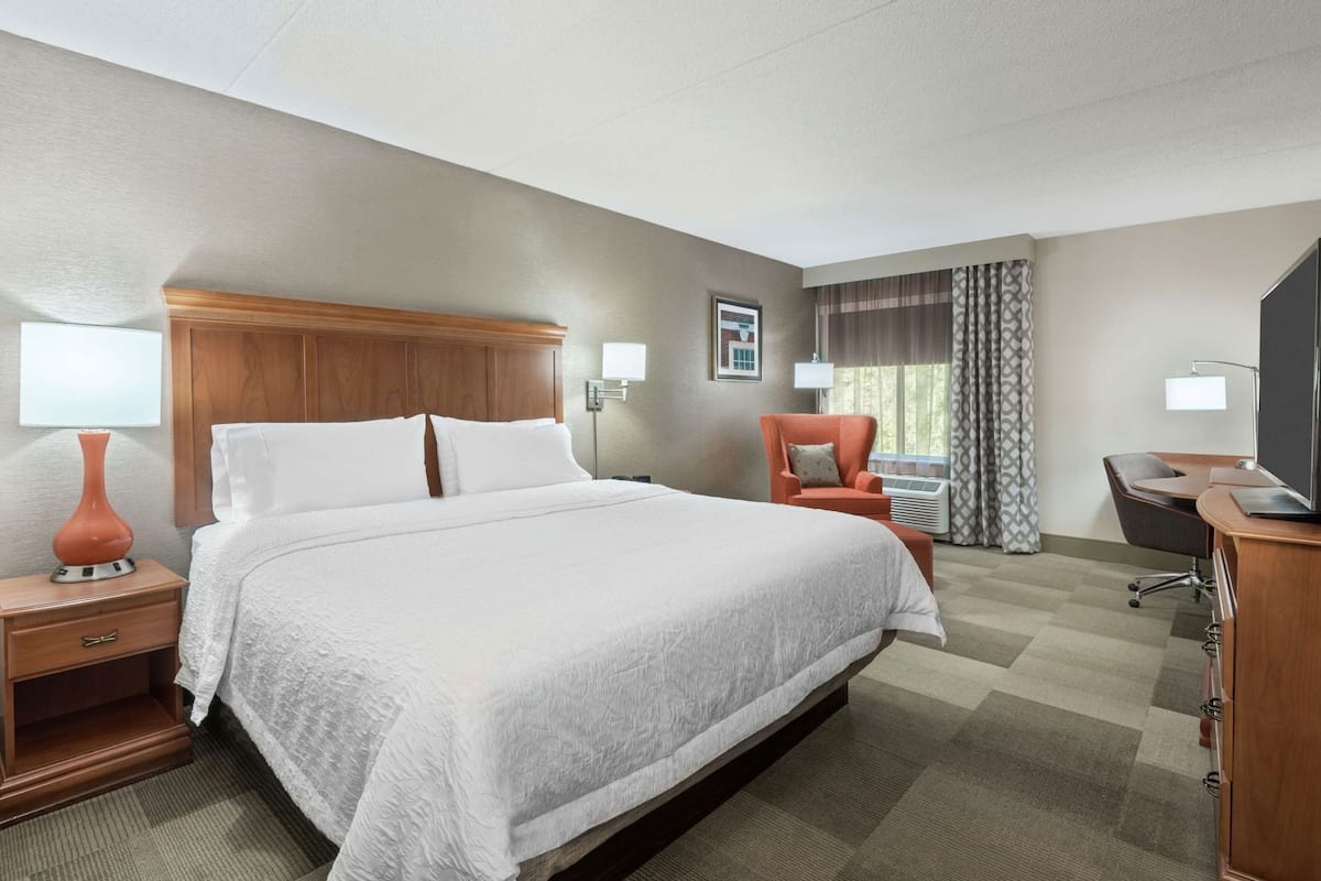 A hotel room with a large bed, a desk, a chair, a TV, and a window with curtains.