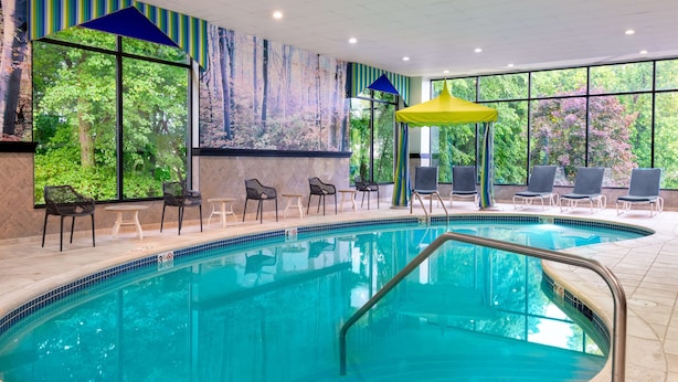 An indoor swimming pool with clear blue water, surrounded by lounge chairs and a large window with a forest view. - Hampton Inn Danbury (Danbury)