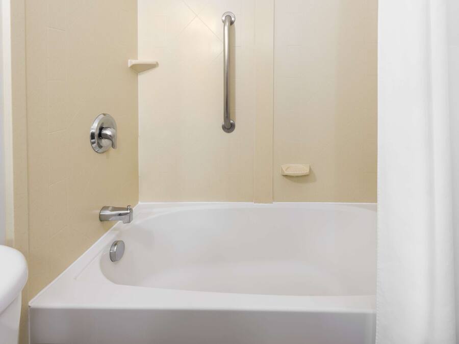 A bathroom with a white bathtub, a handrail, and a toilet.