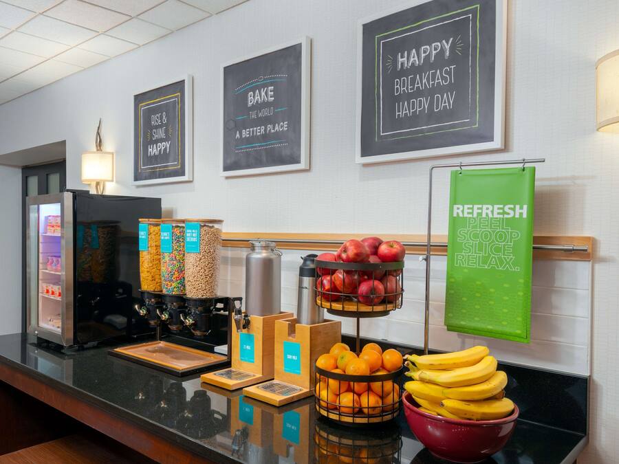 A breakfast bar with a coffee machine, fruit baskets, and a green sign.