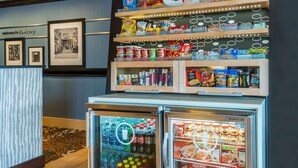 A snack display with various chips and snacks, a refrigerated beverage area, and framed pictures on the wall. - Hampton Inn Danbury (Danbury)