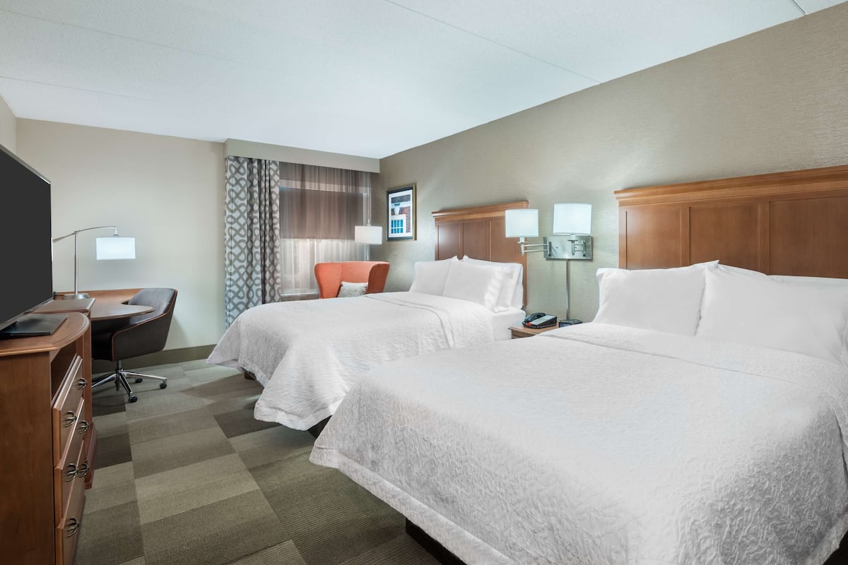 A hotel room with two beds, a desk, a chair, and a TV.