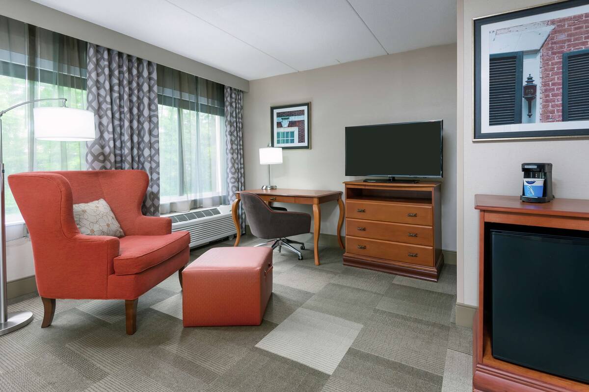 A hotel room with a red armchair, a desk, a television, and a coffee machine.