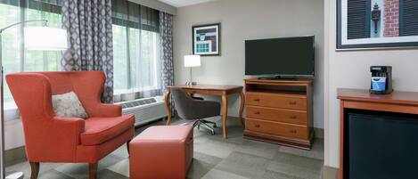 A hotel room with a red armchair, a desk, a television, and a coffee machine.