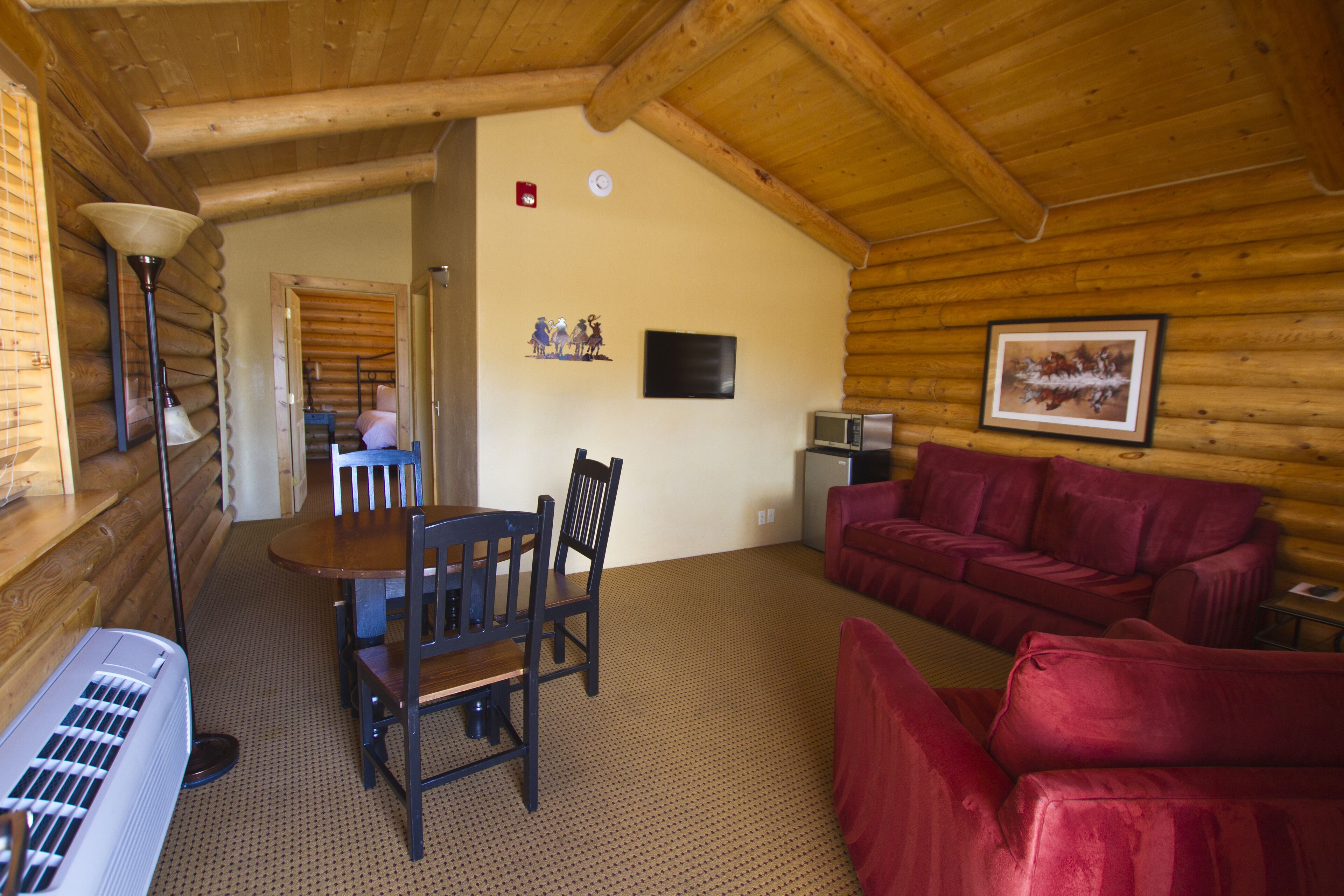 A log cabin interior with a dining area, a red sofa, a television, and a fireplace.