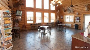 A log cabin-style dining area with multiple tables and chairs, large windows, and mounted animal heads on the walls. - Cody Cowboy Village (Cody)