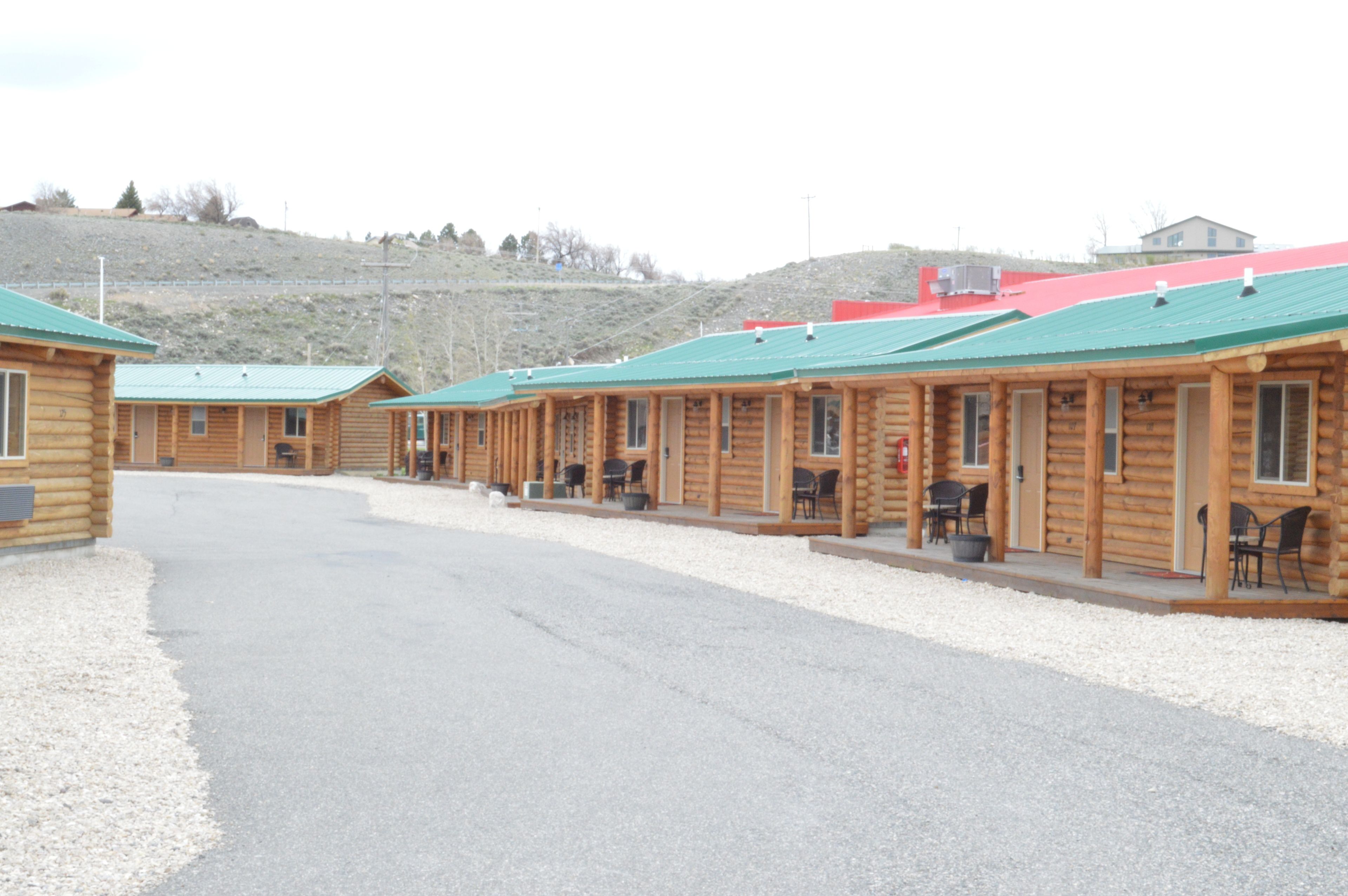 A row of log cabins with green roofs, arranged in a row along a gravel driveway.