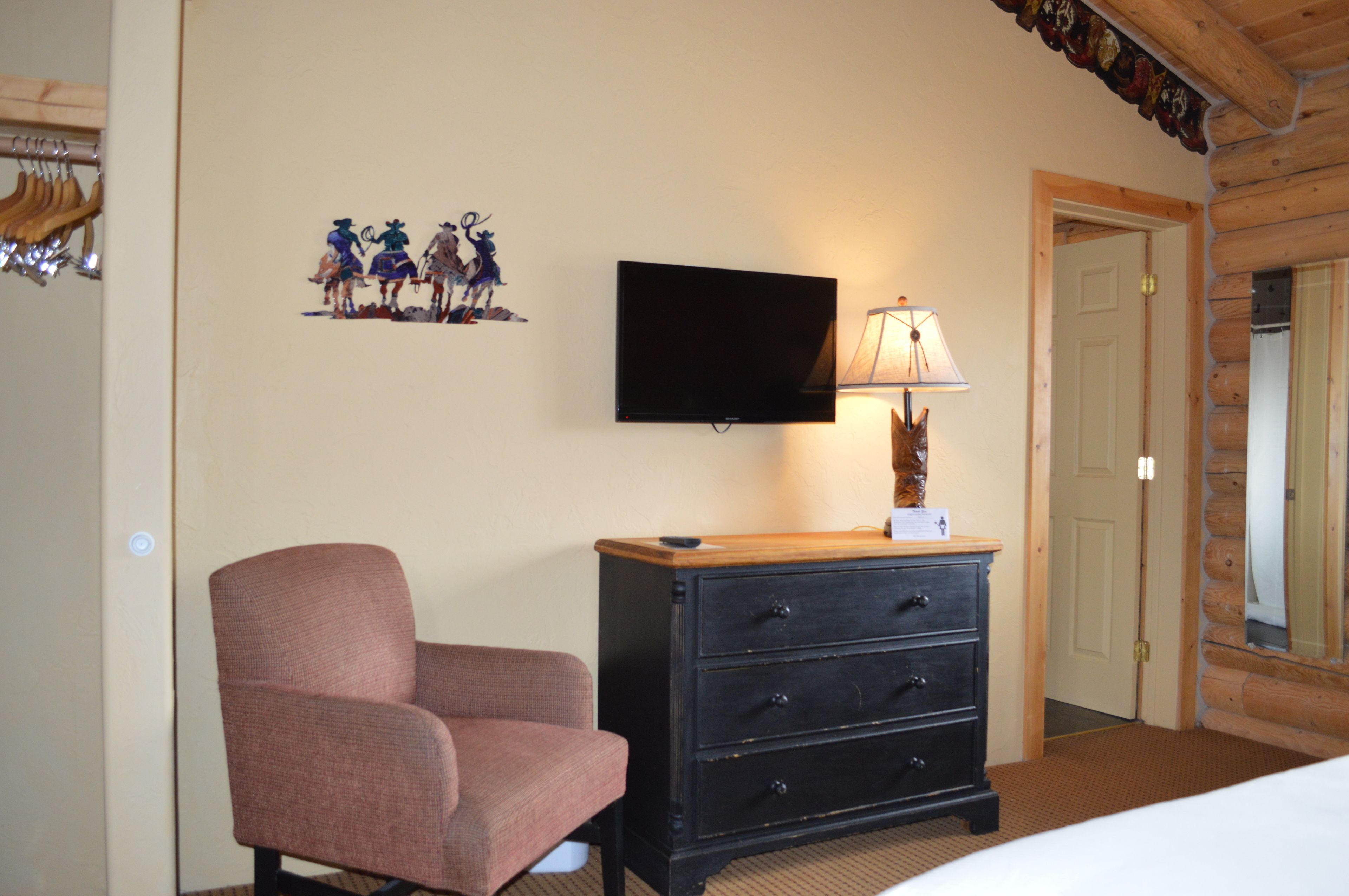 A room with a television mounted on the wall, a wooden dresser, a chair, and a door leading to another room.