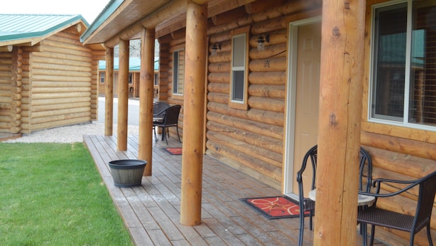 A log cabin with a porch, outdoor seating, and a small garden area. - Cody Cowboy Village (Cody)