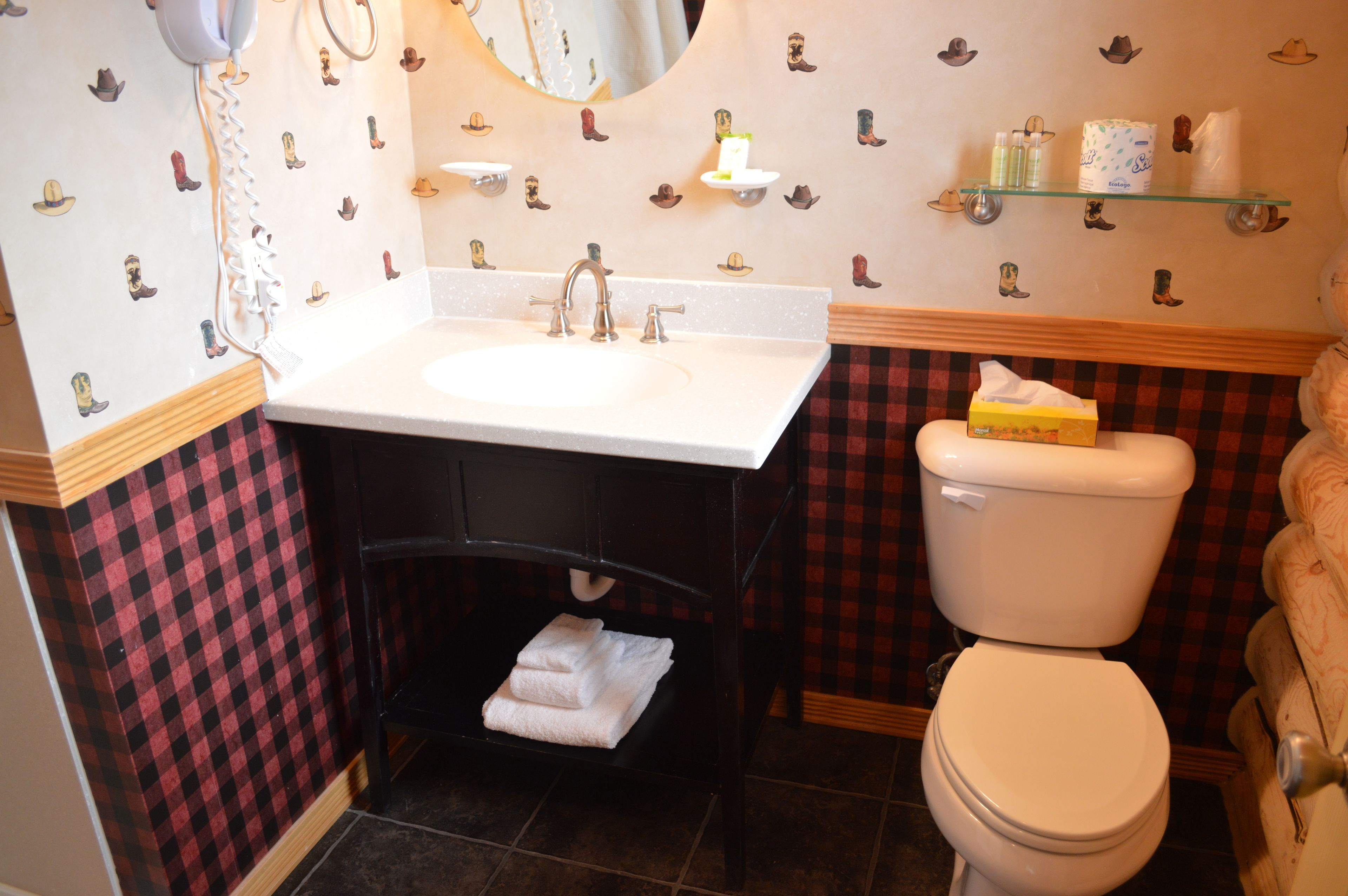 A bathroom with a white sink, black vanity, and a white toilet. There are wall-mounted shelves with toiletries and a mirror above the sink.