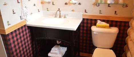 A bathroom with a white sink, black vanity, and a white toilet. There are wall-mounted shelves with toiletries and a mirror above the sink.