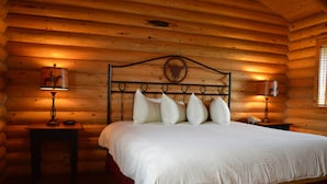 A log cabin room with a wooden bed, two bedside tables, and a lamp on each side. - Cody Cowboy Village (Cody)