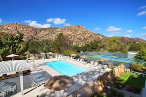 Una piscina con lettini, un campo da tennis e montagne sullo sfondo.
