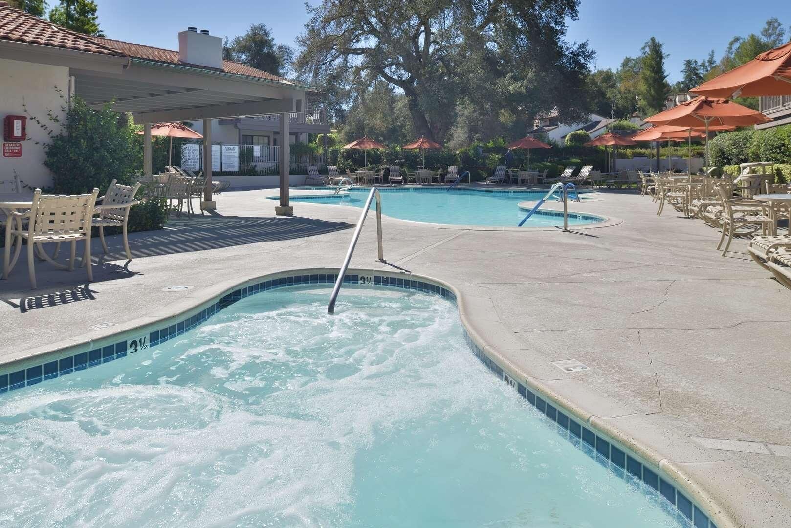 A swimming pool with lounge chairs and umbrellas, surrounded by trees and a building.