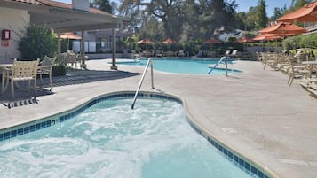A swimming pool with lounge chairs and umbrellas, surrounded by trees and a building.
