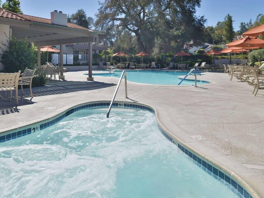 A swimming pool with lounge chairs and umbrellas, surrounded by trees and a building.