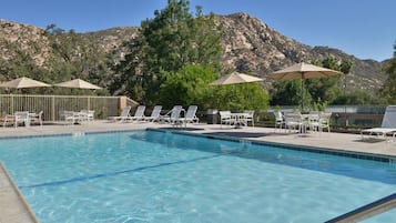 A swimming pool with lounge chairs and umbrellas, surrounded by a fence, with a mountainous backdrop.