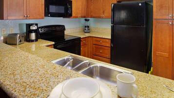 A kitchen with wooden cabinets, a black microwave, a black refrigerator, a coffee maker, and a sink.