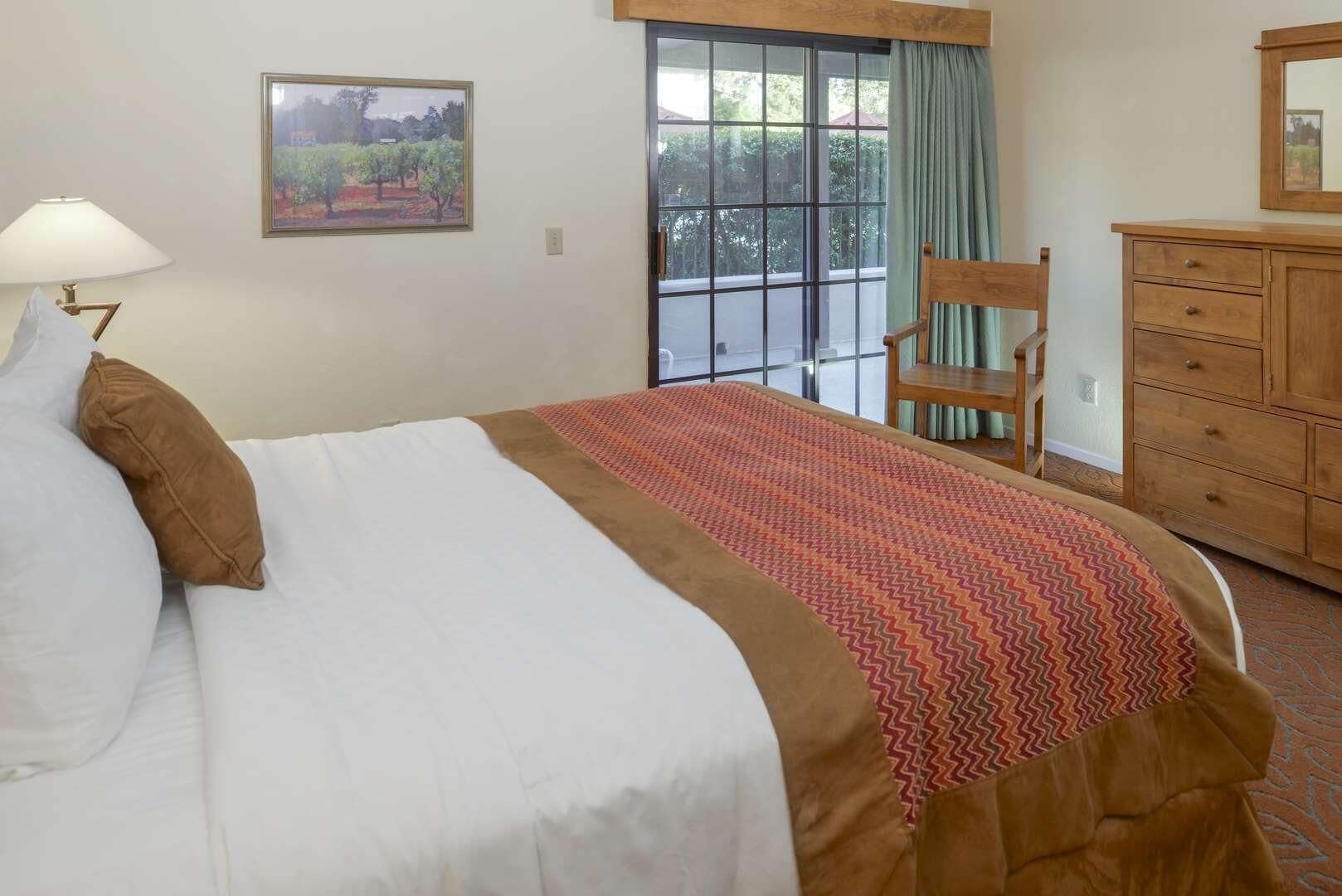 Une chambre d’hôtel avec un lit, une chaise, une commode, une fenêtre donnant sur un paysage agréable et un tableau au mur.