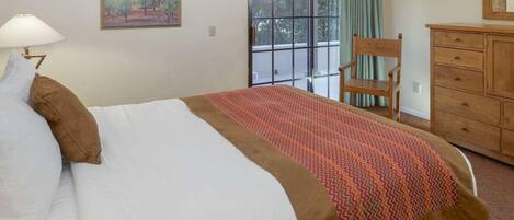 A hotel room with a bed, a chair, a dresser, a window with a view, and a painting on the wall.