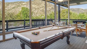 A pool table with a view of a mountainous landscape through large windows.