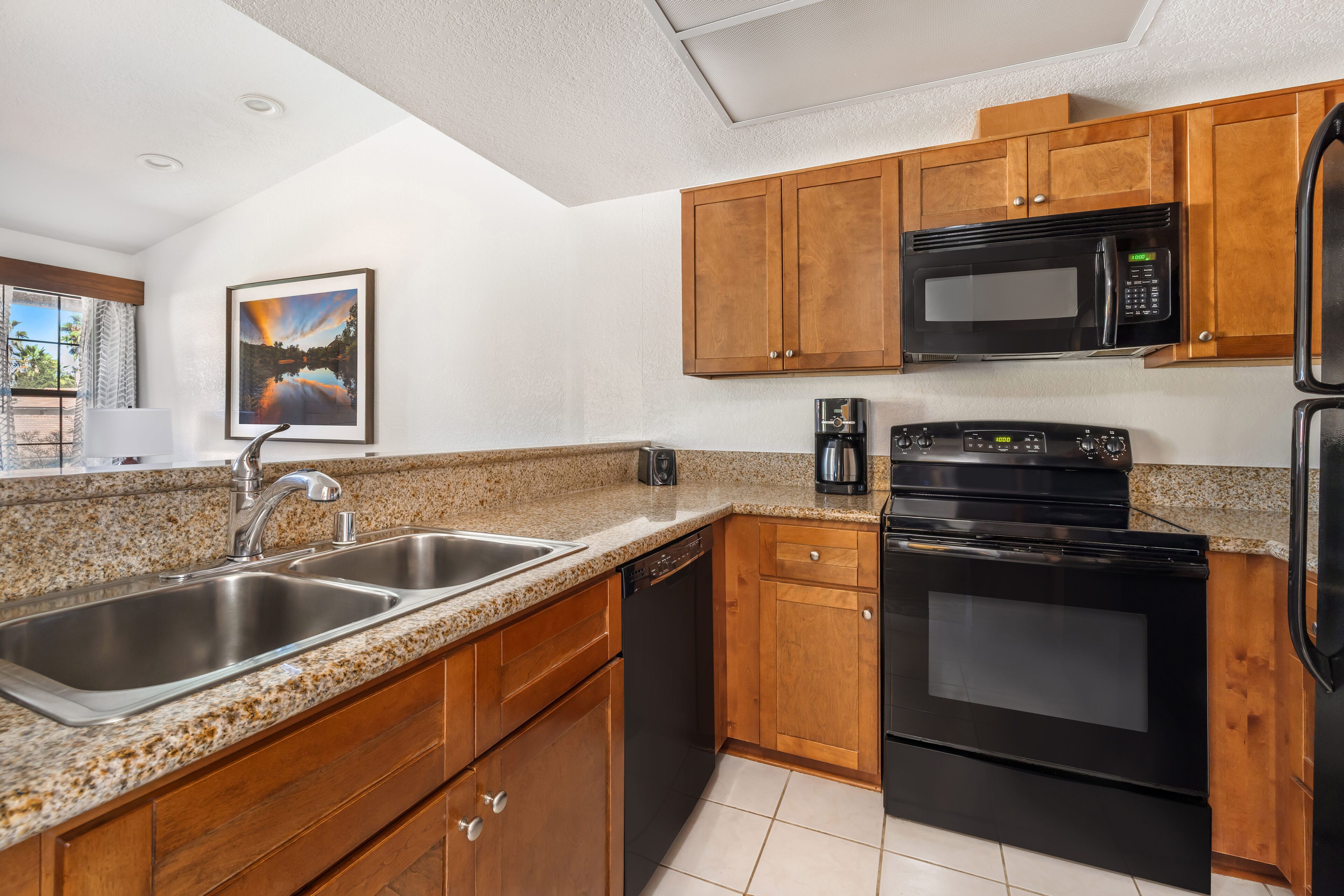 A kitchen with granite countertops, wooden cabinets, stainless steel appliances, and a window with a view.