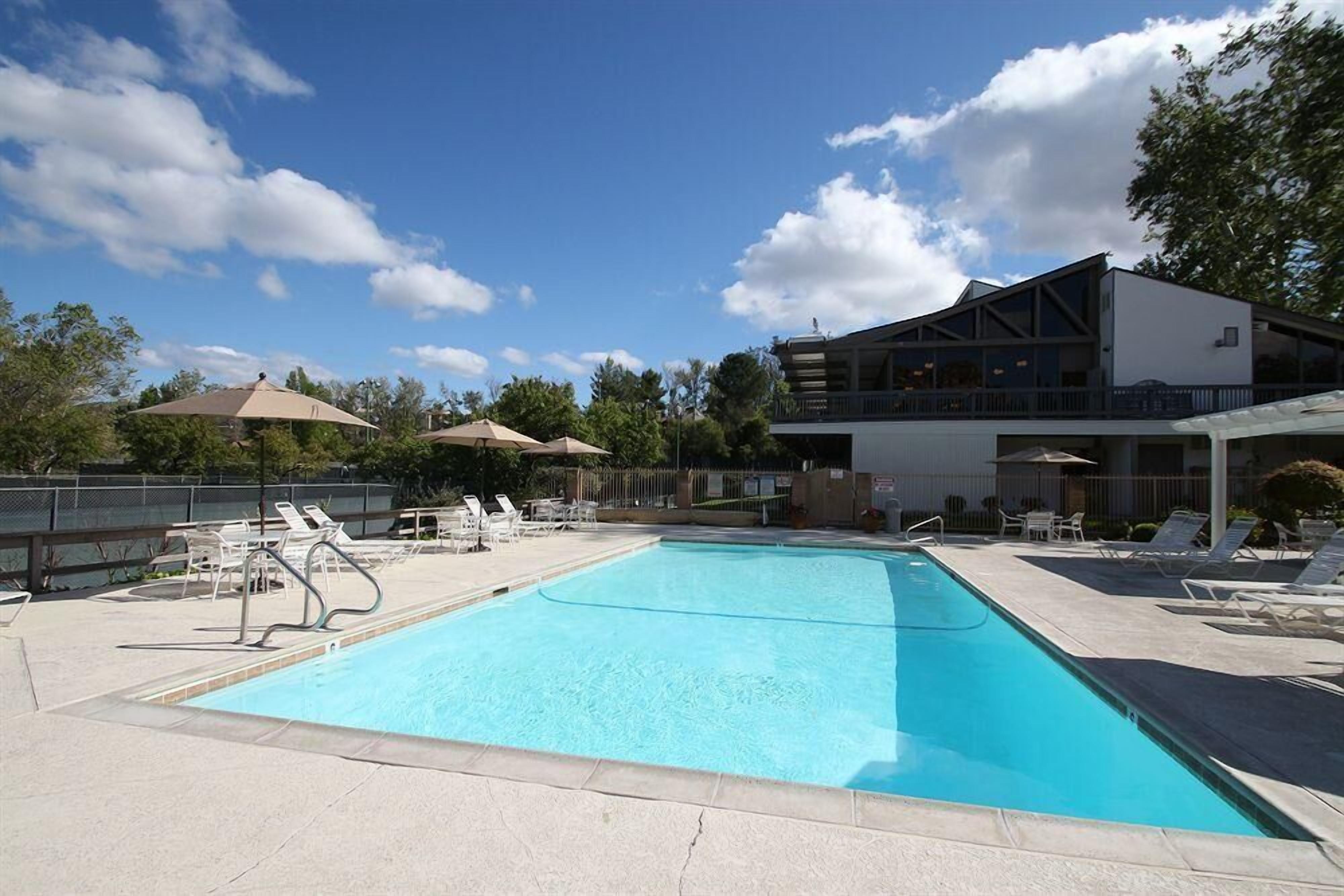 A swimming pool with lounge chairs and umbrellas, a building with a balcony, and a clear sky.