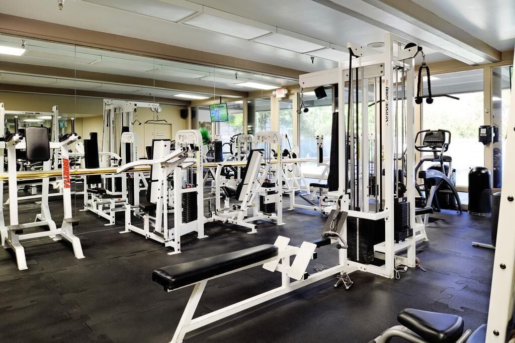 Un gimnasio con diversas máquinas de ejercicio, espejos y una banca.