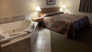 A hotel room with a large bathtub, a bed with a colorful quilt, two bedside lamps, and a framed picture on the wall. - The Upper Pass Lodge at Magic Mountain (Londonderry)