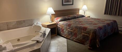 A hotel room with a large bathtub, a bed with a colorful quilt, two bedside lamps, and a framed picture on the wall.