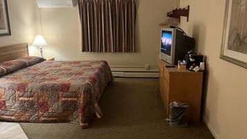 A hotel room with a bed, a television, a desk, and a trash can.