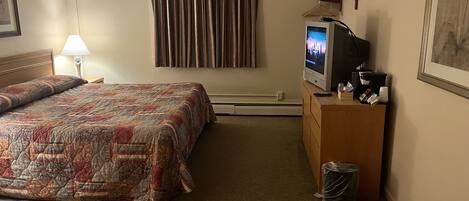 A hotel room with a bed, a television, a desk, and a trash can.