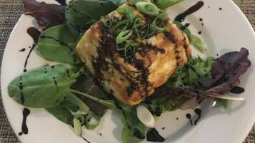 En hvid tallerken med grillet fisk, grønt og en mørk sauce på en strukturret dug.