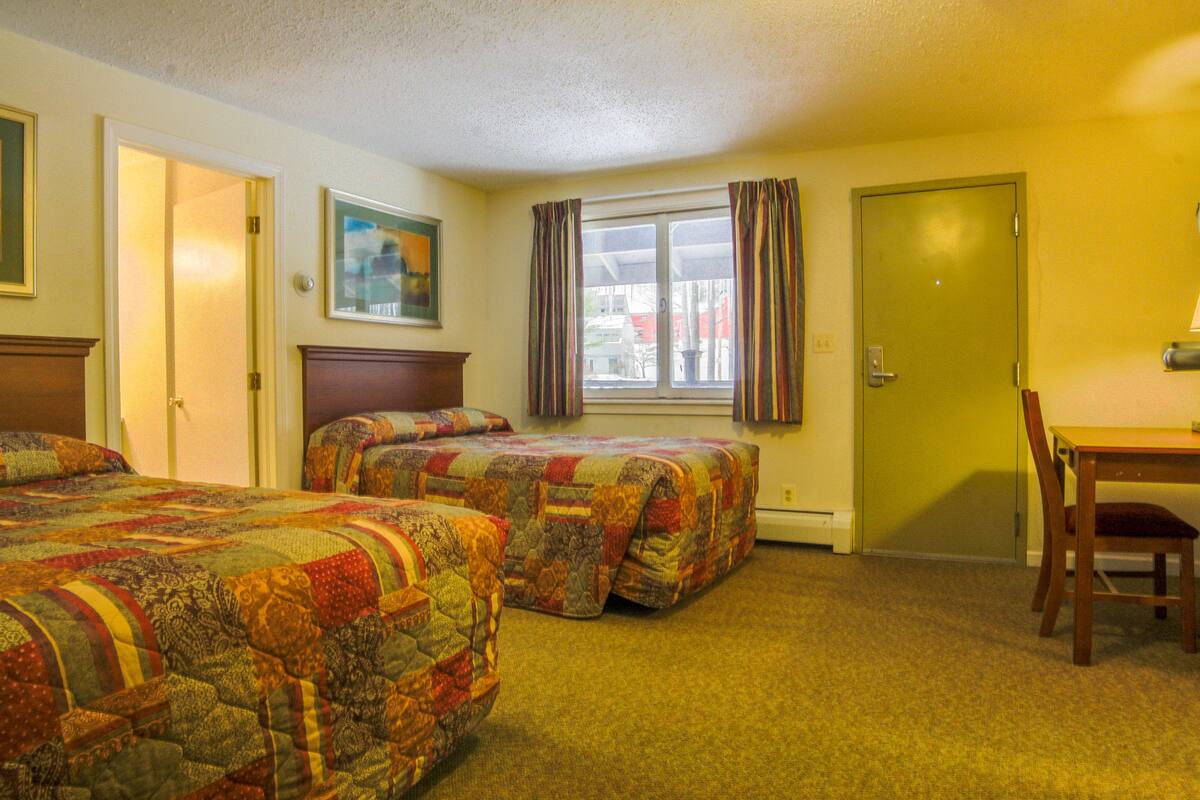 A hotel room with two beds, a desk, and a chair.