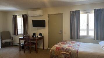 Habitación de hotel con cama, escritorio, silla, televisor y aire acondicionado.